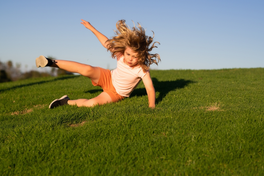 kid runs through the spring grass and falling down on the ground in park