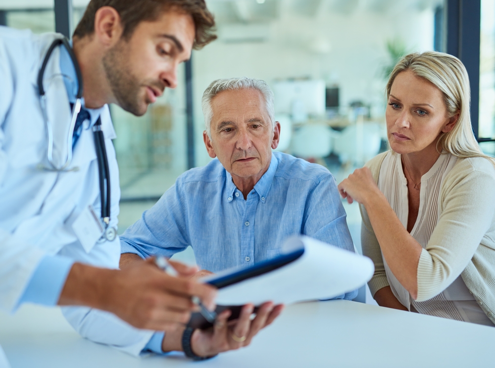 shot of a doctor discussing some paperwork with a senior patient and his daughter in a clinic